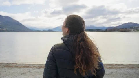 Woman standing with back to camera looking at beautiful lake waters in cold day Stock Footage 289416559
