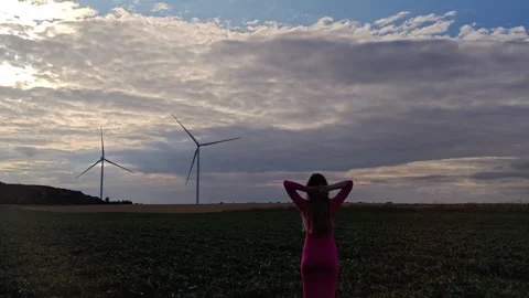 Woman standing back to camera looking at wind turbines in green field Stock-Footage 341130026