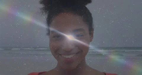 Woman standing on beach facing camera smiling lens flare entering left creating Stock Footage 329533953