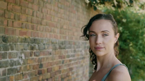 Woman standing by a brick wall while looking straight at the camera and smiling Stock Footage 130253799