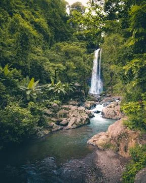 Woman standing in the distance in front of huge waterfall in Bali, Indonesia. Stock Photos