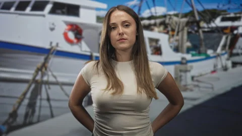 Woman standing with hands behind back in front of a docked boat at a marina.. Stock Footage 337430126