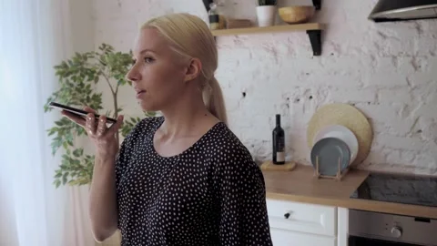 Woman standing in home kitchen having fun chatting with friend use speaker phone Stock Footage 136401883