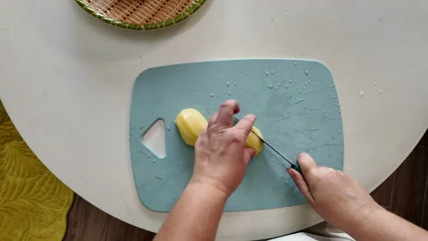 A woman standing at the kitchen table cuts potatoes for lunch with a sharp knife Stock Footage 319328245