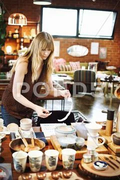 Woman standing in a shop, arranging merchandise on a table. Stock Photos