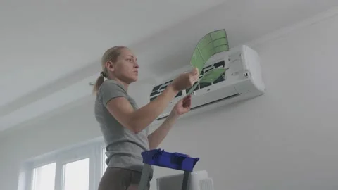 A woman standing on a stepladder pulls the air filter out of the split system Stock Footage 143544807