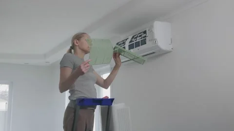 A woman standing on a stepladder pulls the air filter out of the split system Stock Footage 143567338
