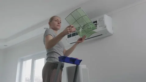 A woman standing on a stepladder pulls the air filter out of the split system Stock Footage 146095566