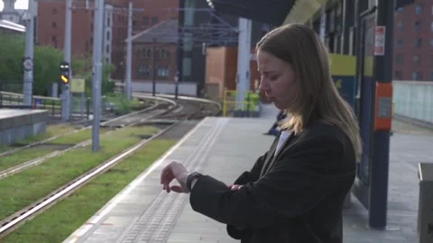 Woman standing at tram stop looking at her watch waiting for the tram to arrive Stockbeeldmateriaal 276663243