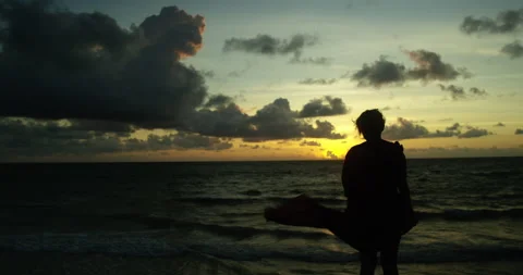 Woman stands by ocean looking at dramatic sunset Vídeo Stock 139376817