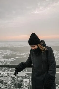 Woman stands on a pier overlooking ice-covered water during sunset Stock Photos