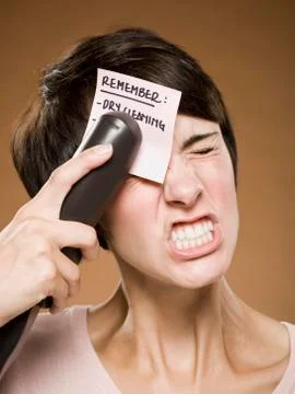 Woman stapling list of things to remember to her forehead and wincing 写真素材