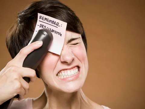 Woman stapling list of things to remember to her forehead and wincing 写真素材