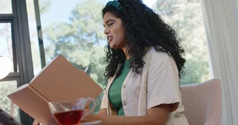 Woman starting with tan folder, reading aloud and turning pages at home beside Stock Footage 345065774