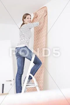 Woman sticking wallpaper on wall Stock Photos