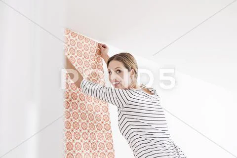 Woman sticking wallpaper on wall, smiling Stock Photos