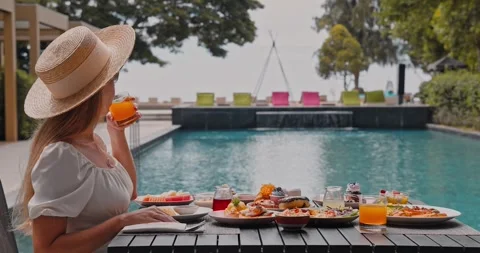 Woman in straw hat drinking orange juice by resort swimming pool Видео 332775271