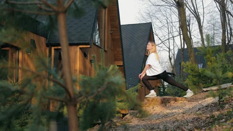 Woman stretching outside a rustic cabin in the woods. A woman in athletic wear Stock Footage 284844290
