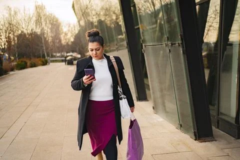 Woman strolling outdoors while checking her smartphone on a sunny day Stock Photos