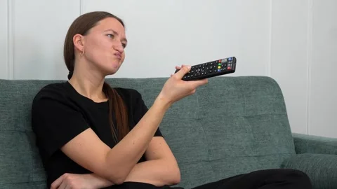 Woman struggling with remote control, changing channels on sofa Stock Footage 307293126