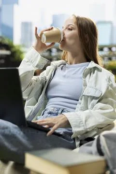 Woman student drinking coffee while working on laptop on beanbag Stock Photos