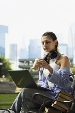 Woman student drinking coffee while working on laptop on bench Stock Photos