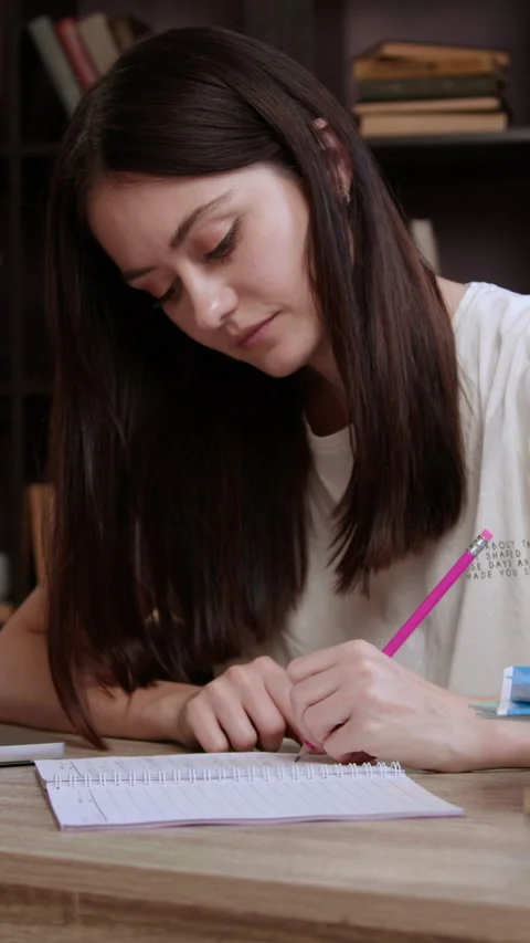 Woman student notes down summary of online presentation sitting at desk in Stock Footage 305407118