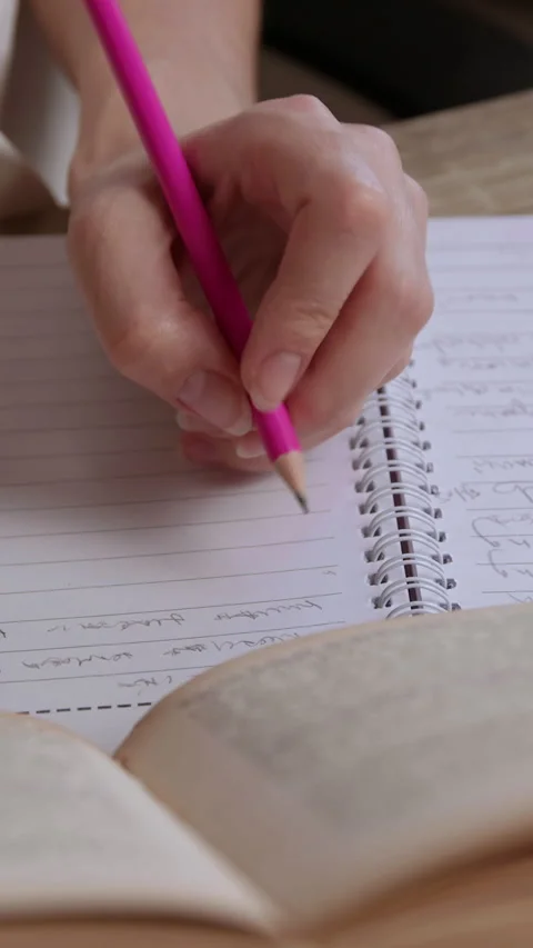Woman student writes notes by left hand with pink pencil in notebook using Stock Footage 305408006