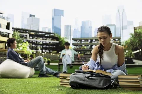 Woman student writing down notes from open book during study time Stock Photos