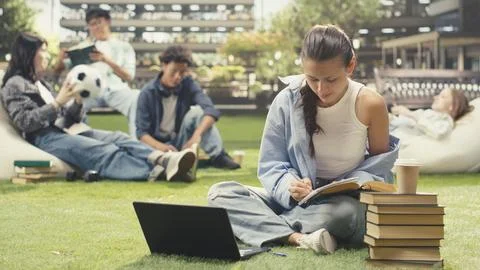 Woman student writing down notes from open book during study time Stock Photos