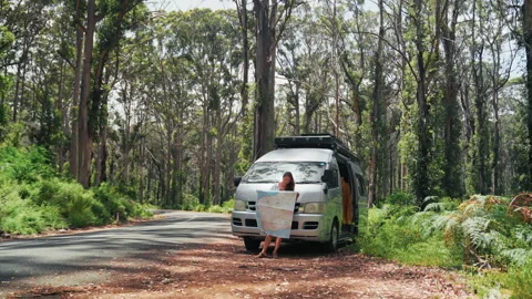 Woman studies map beside camper van on forest road Video stock 330773653