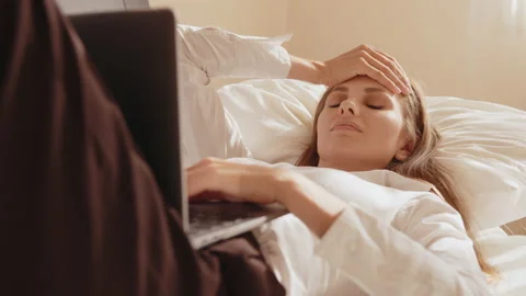 Woman suffering from headache while using laptop on bed Stock Footage 164497520