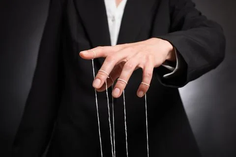 Woman in suit pulling strings of puppet on dark background, closeup Stock Photos