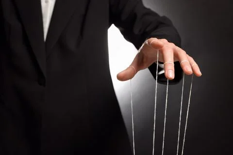 Woman in suit pulling strings of puppet on dark background, closeup Stock Photos