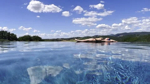 Woman sunbathing on edge of infinity pool with countryside view Stock Footage 342344228