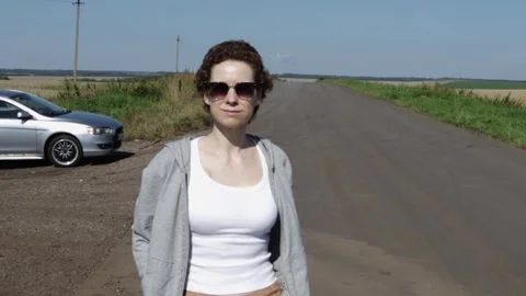 Woman in sunglasses looking along an empty rural road beside her parked car.. Stock Footage 345412260