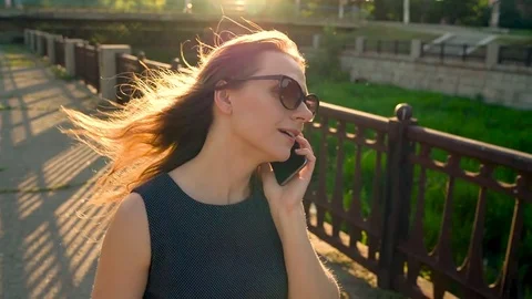 Woman in sunglasses talking on the smartphone while walking down the street at Stock Footage