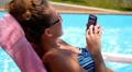 Woman Surfing Internet in the Phone while Relaxing in Pool near Hotel. HD Footage