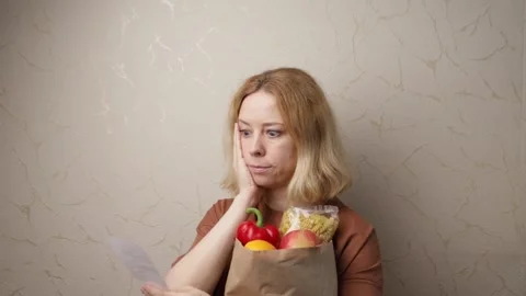 Woman surprised by food prices, looking at grocery receipt, shocked by rising co Stock Footage 262946751
