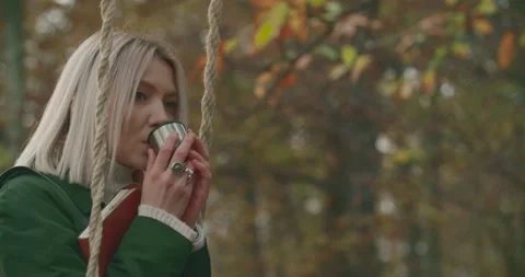 Woman swinging while drinking hot tea in the middle of a cold park in autumn Stock-Footage 140898360