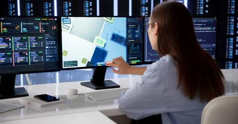 Woman Systems Engineer Monitors Multiple Server Data Screens At Workspace. Stock Photos