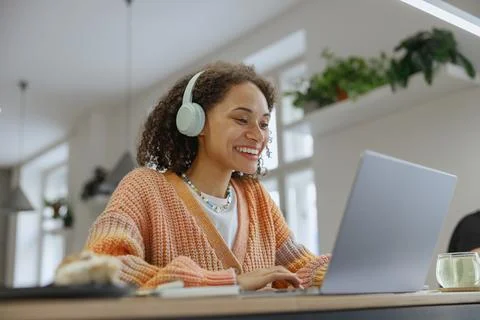 A woman at a table using a laptop computer with headphones on Stock Photos