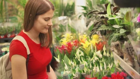 Woman takes closer look at array of indulging flowers before picking up pot to Stock Footage