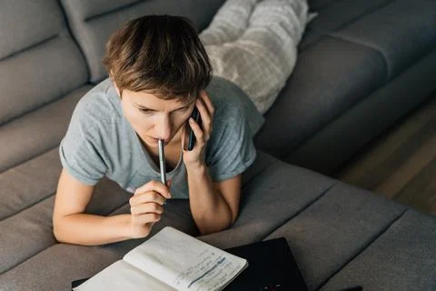 Woman takes notes while talking on her cell phone in her home clothes Stockfoto's