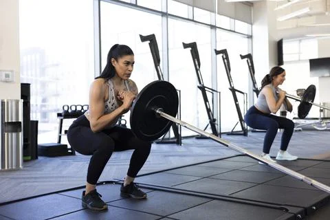 Woman taking a deep breath while doing barbell squats in gym Stock Photos