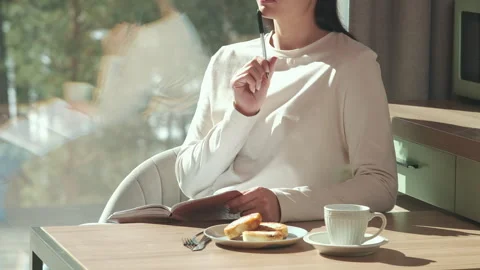 Woman taking notes and having breakfast in a modern kitchen Stock Footage 303499577