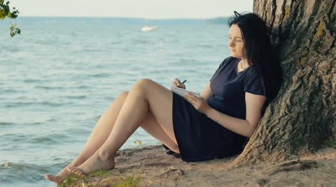 Woman taking notes in a notebook sitting on the coast Vídeo Stock 65826720