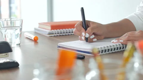 A woman is taking notes in a notebook, sitting at a table Vídeo Stock 141343848