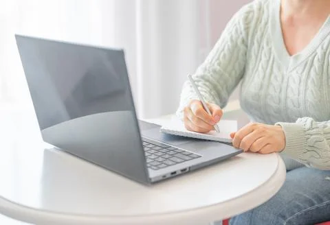 Woman taking notes in notebook while using laptop with at home. freelancer wr Stock Photos