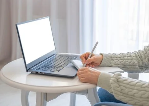 Woman taking notes in notebook while using mockup laptop with blank white scr Stock Photos